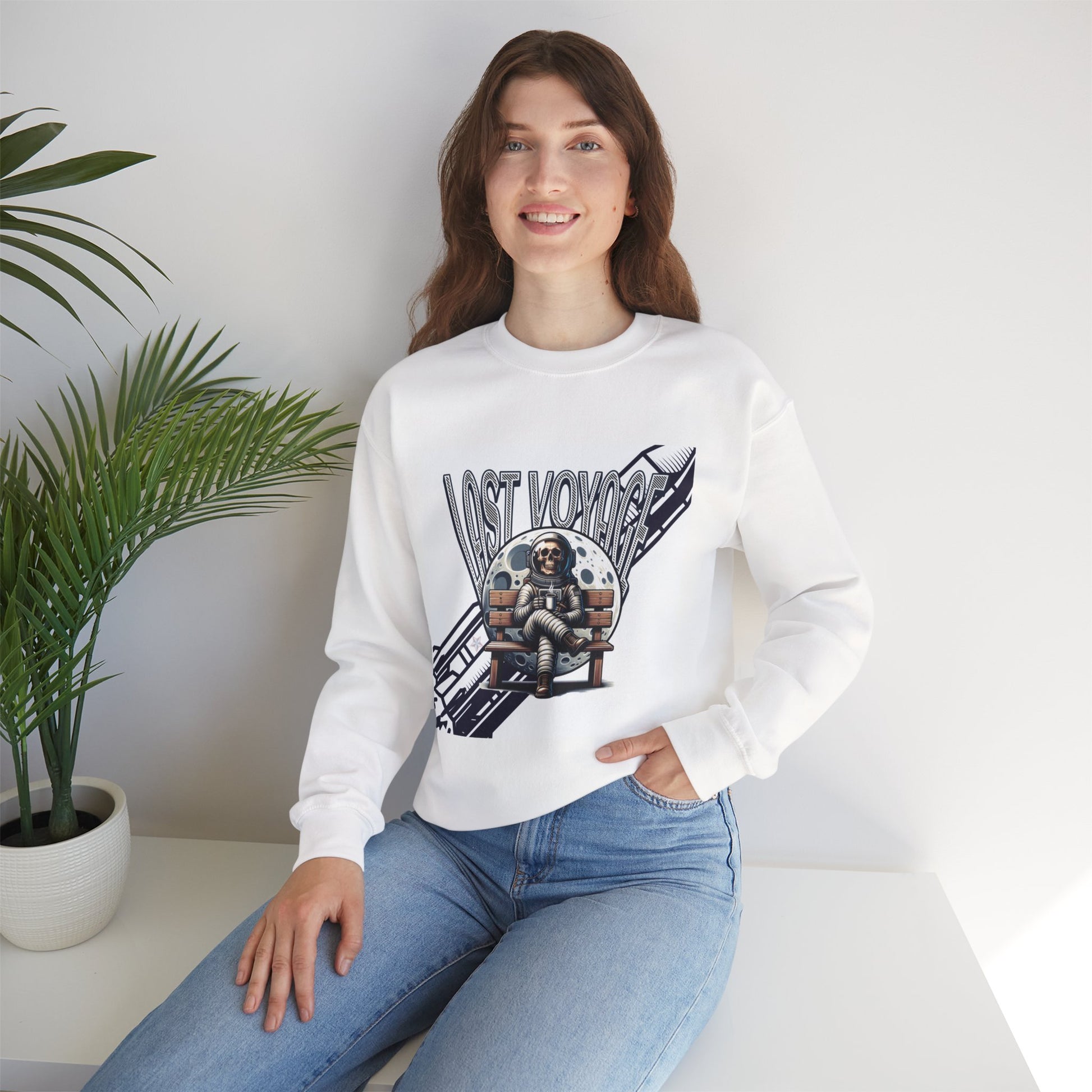 Person wearing a white sweatshirt with a graphic design sitting on a white surface with a plant in the background.