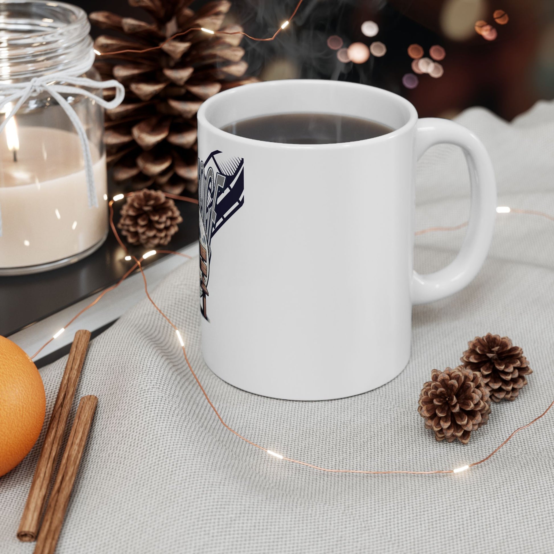 White mug with a logo on a table with decorative items including pine cones and an orange.