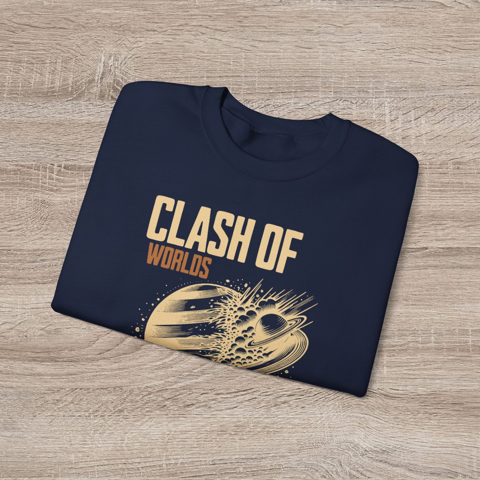 Folded navy blue sweatshirt with 'Clash of Worlds' text and graphic on a wooden surface