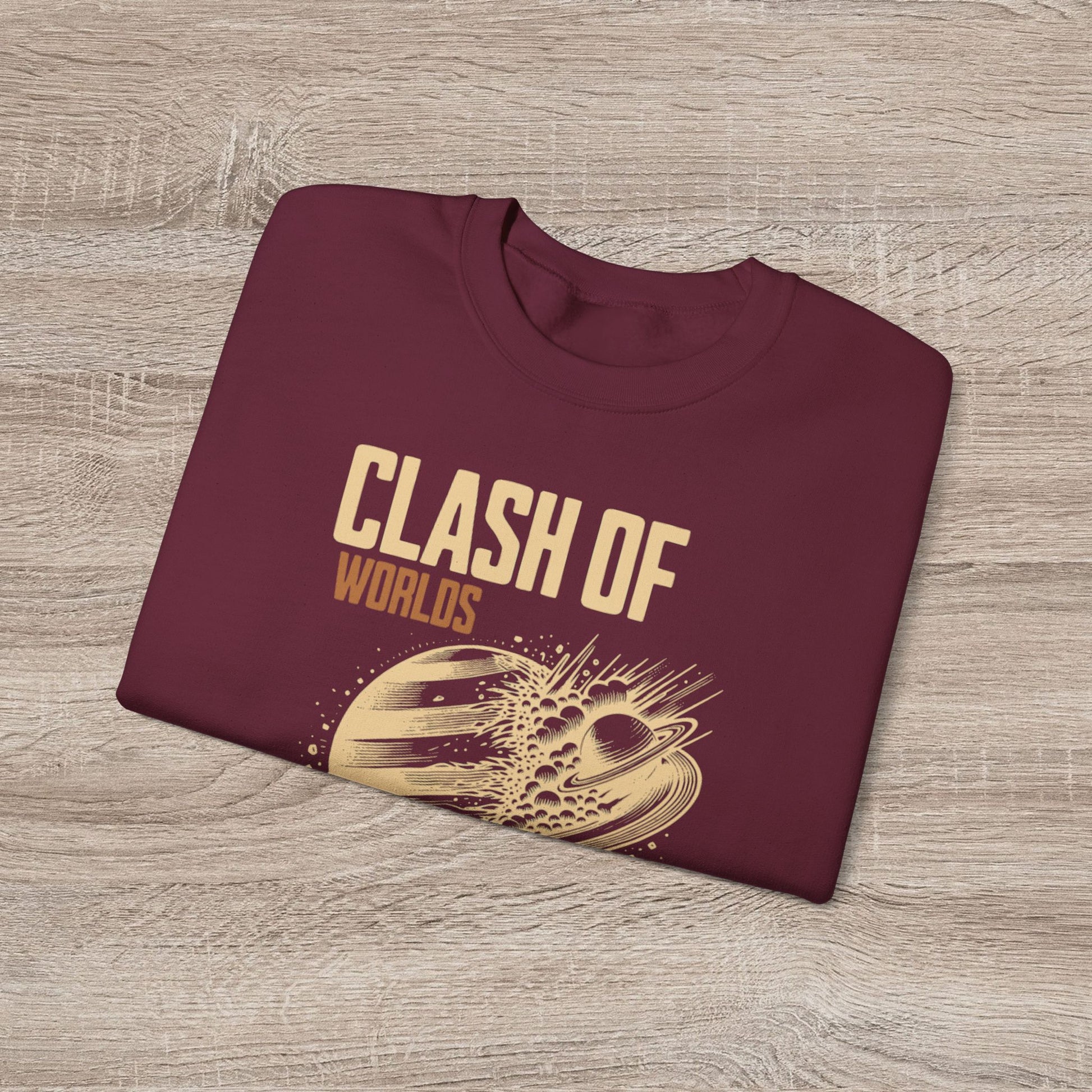 Folded maroon sweatshirt with 'Clash of Worlds' text and graphic on a wooden surface